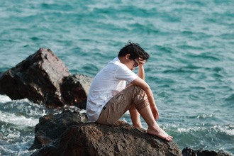 海辺で落ち込む男性
