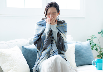 ソファに座ってブランケットを肩から羽織って体調の悪そうな女性